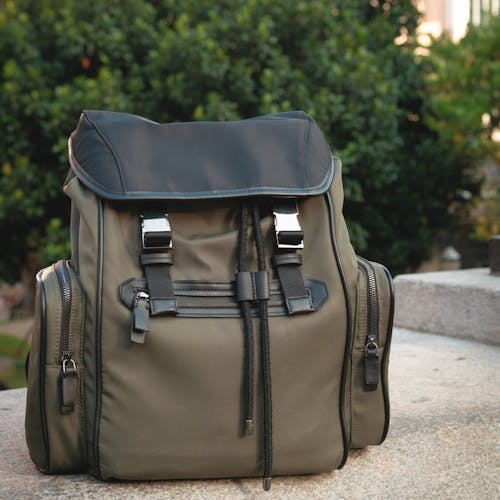 Modern olive green backpack with leather details sitting outdoors on stone. Perfect for travel or fashion look.